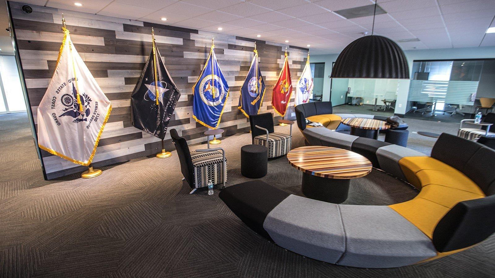 An image of 满帆’s 军事 Student Success center shows a large couch, 小型会议室, 和 flags representing each branch of the US Armed Services.
